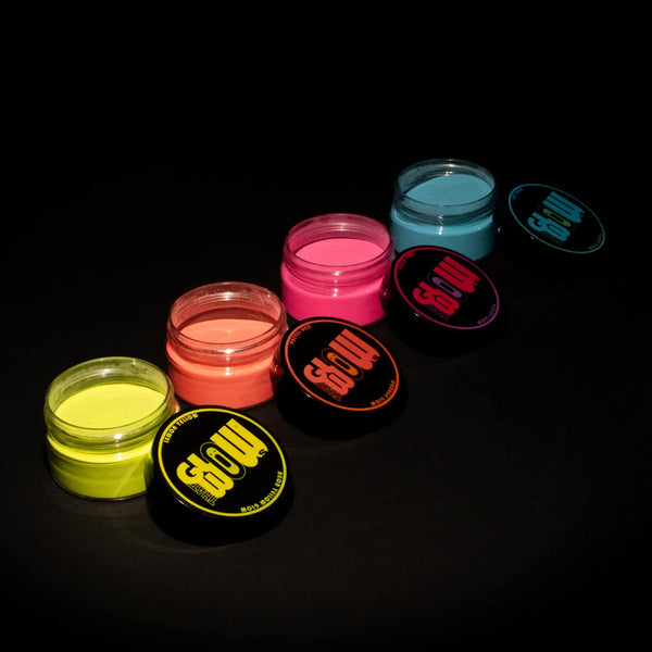 Top-down view of four glow pigment powder jars—green, orange, purple, blue—with matching black lids beside them, perfect for painting rocks, clothing accents and epoxy resin projects